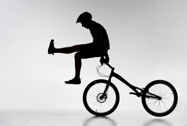 silhouette of trial cyclist standing on handlebars with hands on white