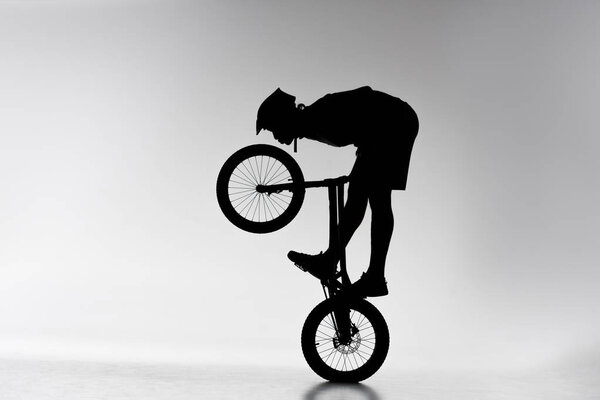 silhouette of trial biker performing balancing stunt on bicycle on white