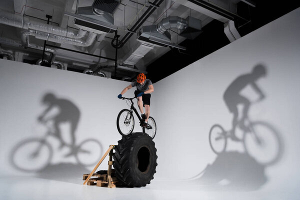 young athletic trial biker balancing on tractor wheel