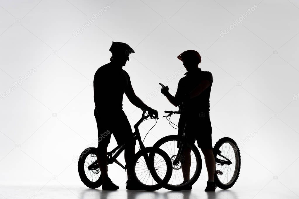 silhouettes of trial bikers with bicycles chatting on white