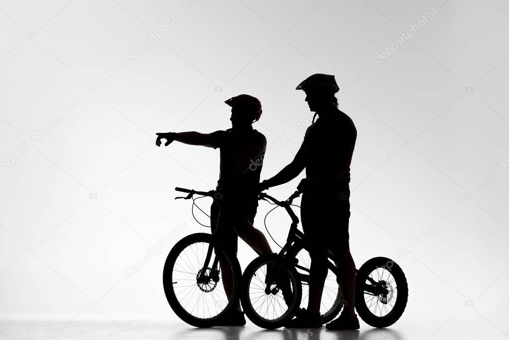 silhouettes of trial cyclists with bicycles chatting on white