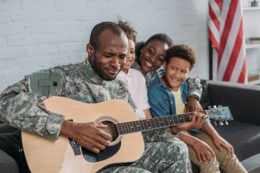 Afrikalı-Amerikalı kadın ve çocuk babası kamuflaj giysili gitar çalmaya dinlerken