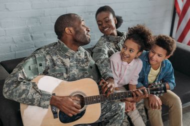 Afrikalı-Amerikalı kadın asker ve kamuflaj baba dinlerken çocuklar elbise gitar çalmak