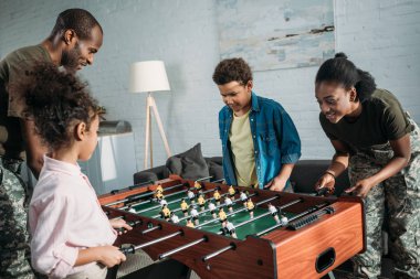 Onların çocukları ile masa futbolu oynayan Afrikalı-Amerikalı erkek ve kadın askerler