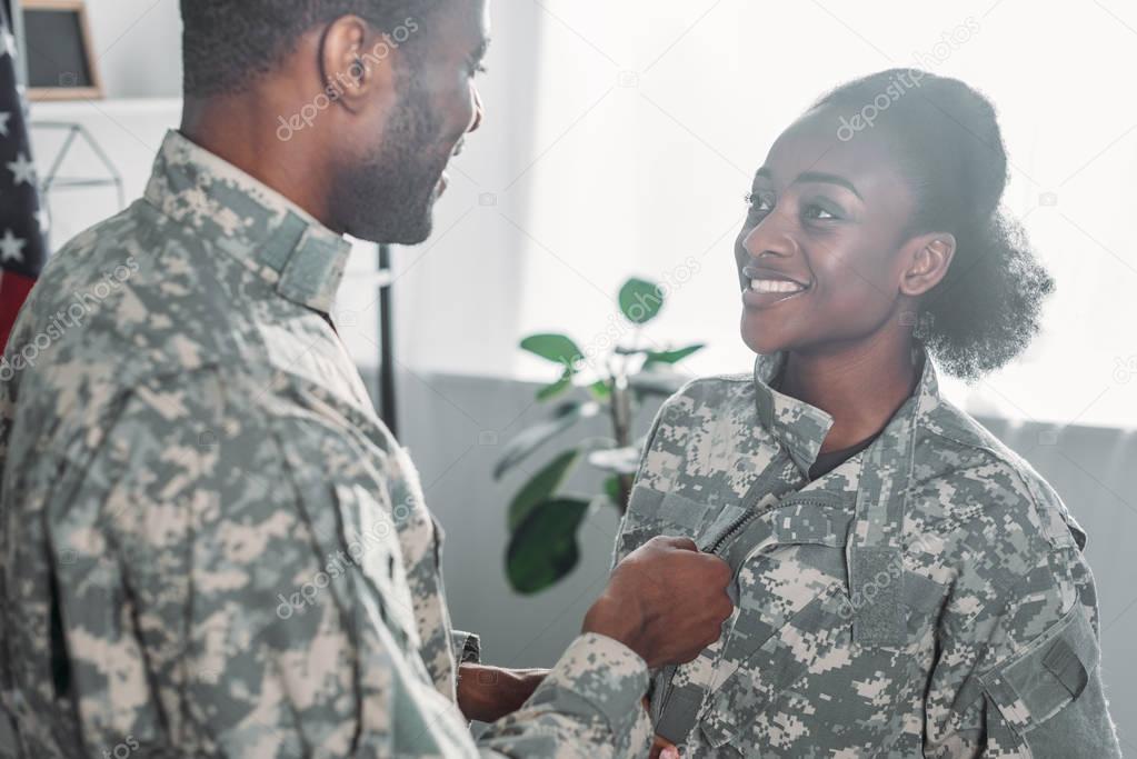 Male soldier helping woman to get dressed in camouflage clothes