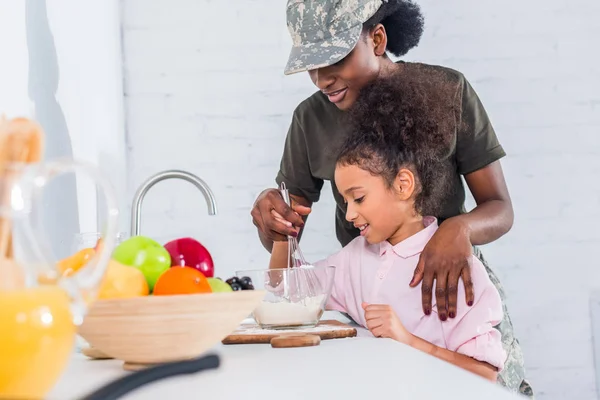 自宅キッチンで料理一緒に小さな娘とアフリカ系アメリカ人の兵士  — 無料ストックフォト