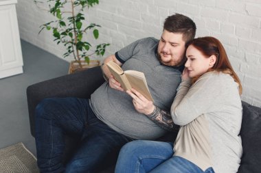 boyfriend and girlfriend reading book together on sofa in living room clipart