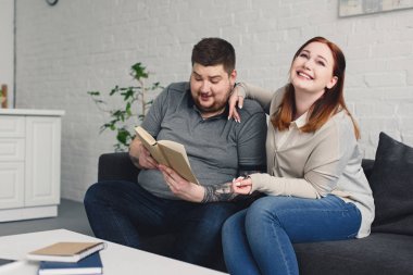 boyfriend reading book to smiling girlfriend at home clipart
