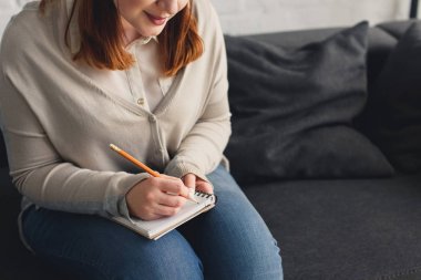 Cropped image of size plus girl writing something to notebook at home clipart