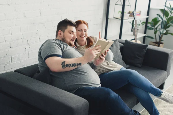 Sorridente Fidanzato Sovrappeso Fidanzata Lettura Libro Sul Divano Casa — Foto Stock