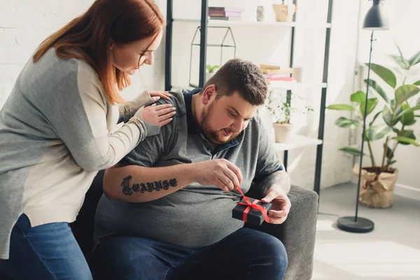 Girlfriend presenting gift to overweight boyfriend at home