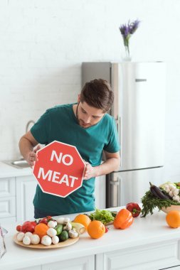 handsome vegan man looking at no meat sign in kitchen clipart