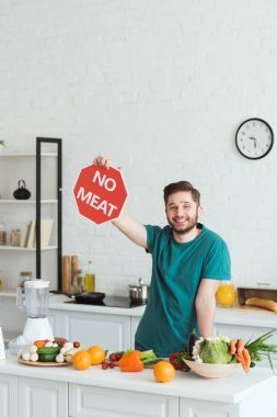 smiling handsome vegan man holding no meat sign in kitchen clipart