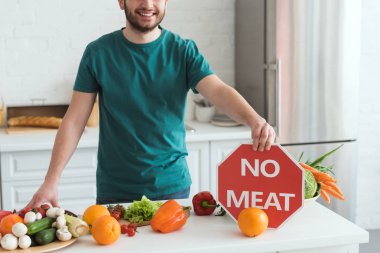 cropped image of handsome vegan man holding no meat sign in kitchen clipart