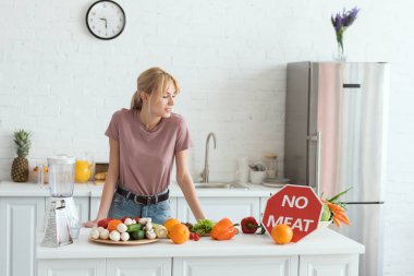 attractive vegan girl looking at no meat sign in kitchen clipart