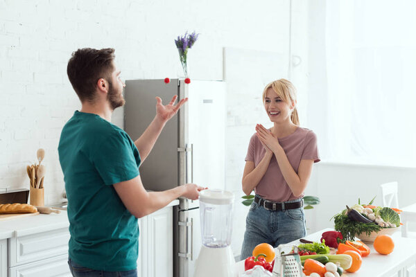 vegan boyfriend juggling with cherry tomatoes for happy girlfriend at kitchen