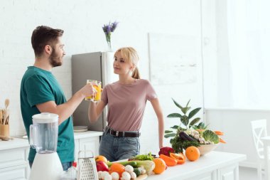 couple of vegans clinking with glasses of orange juice at kitchen clipart