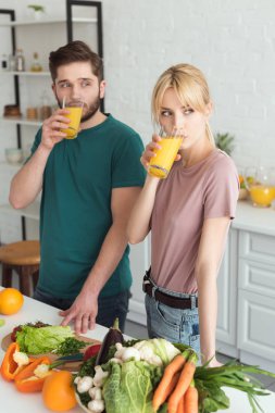couple of vegans drinking fresh juice at kitchen and looking away clipart