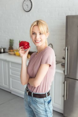 Mutfakta biber tutarak ve kameraya bakarak çekici vegan kız