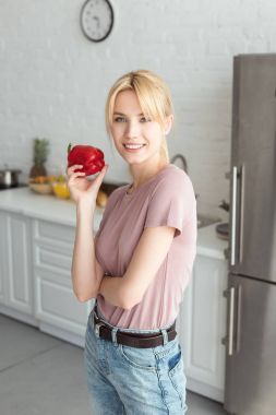 attractive vegan girl holding bell pepper in kitchen and looking at camera clipart