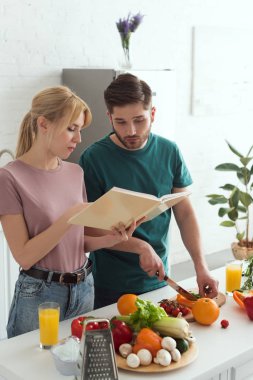 couple of vegans preparing food with cookbook at kitchen clipart