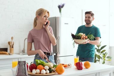 vegan girlfriend talking by smartphone while cooking at kitchen clipart
