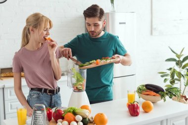 young couple of vegans preparing vegetable juice at kitchen clipart