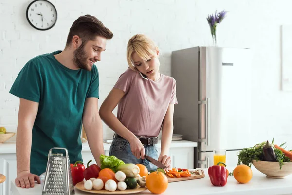 キッチンがあり 食事を準備しながらスマート フォンで語っている菜食主義者のガール フレンド — ストック写真