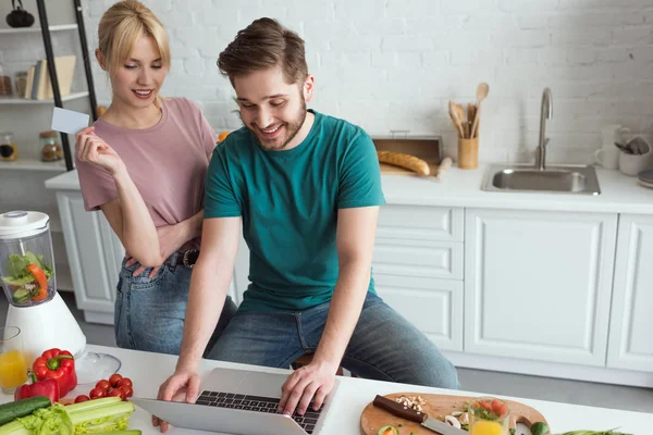 vegan couple with laptop buying goods online together in kitchen at home