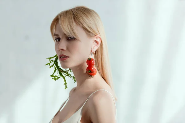 thoughtful woman in dress with earrings made of fresh arugula and cherry tomatoes, vegan lifestyle concept