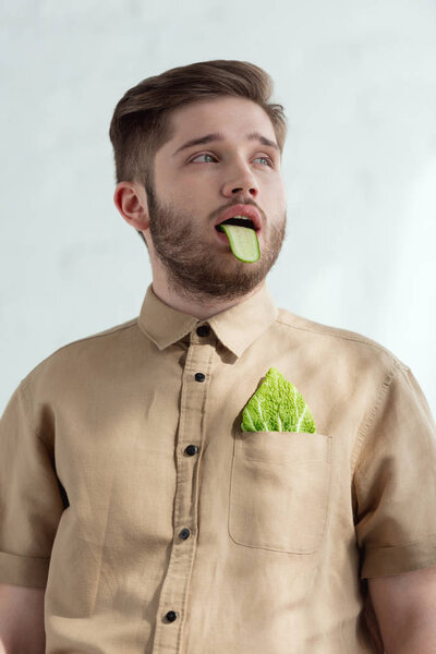 portrait of man with cucumber slice in mouth and savoy cabbage leaf in pocket, vegan lifestyle concept 