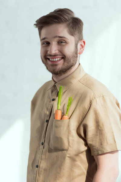 portrait of smiling bearded man with fresh carrots in pocket, vegan lifestyle concept