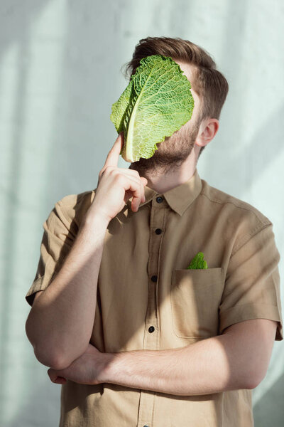 obscured view of pensive man with savoy cabbage leaf on face, vegan lifestyle concept
