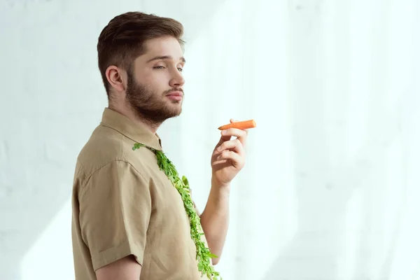 side view of young man with tie made of arugula and carrot as cigarette, vegan lifestyle concept