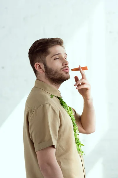 side view of young man with tie made of arugula and carrot as cigarette, vegan lifestyle concept