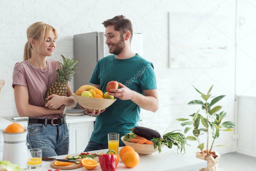 young vegan couple with fresh fruits and vegetables in kitchen at home