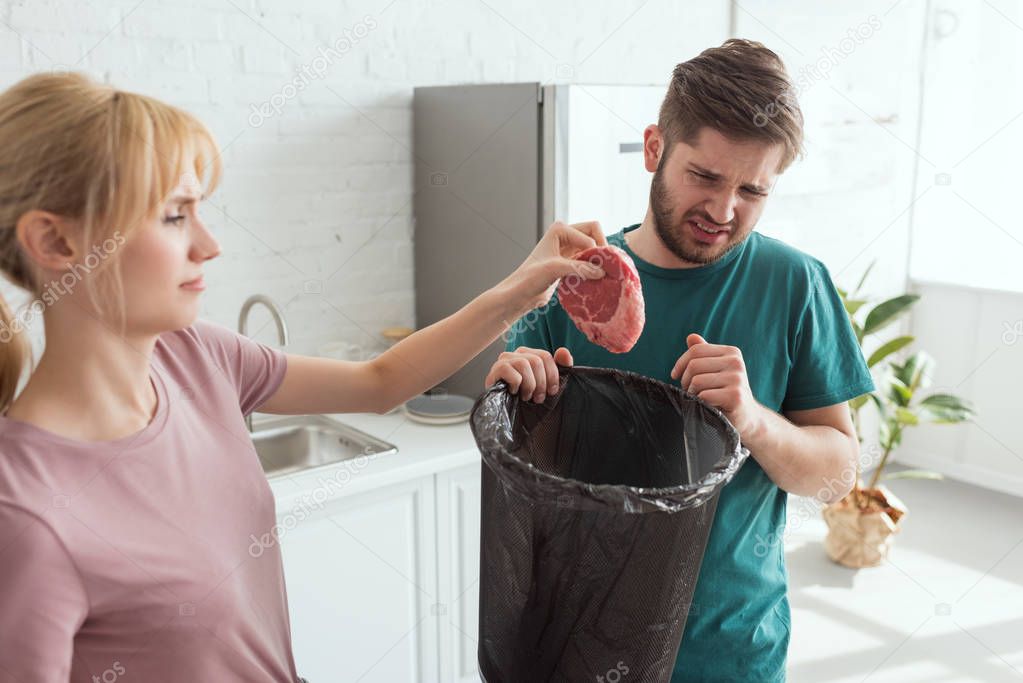 couple throwing away raw meat in kitchen at home, vegan lifestyle concept