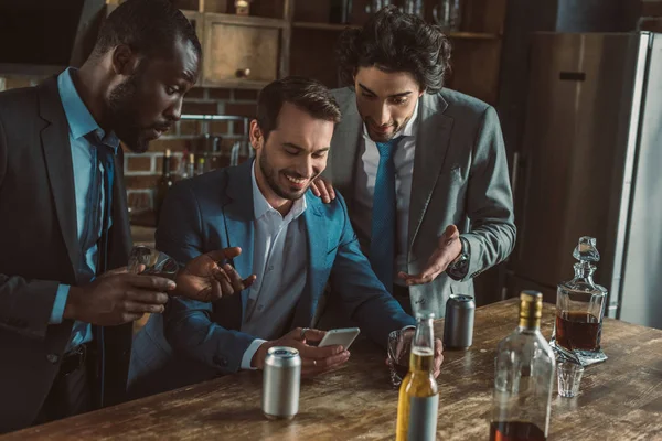 微笑的多民族男性朋友在西装使用智能手机和饮用酒精饮料一起 — 图库照片