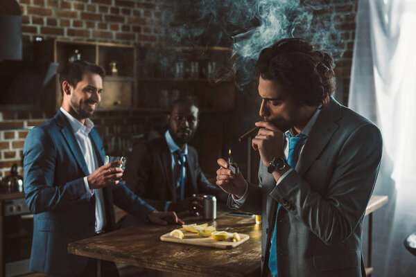 handsome young businessman smoking cigar while smiling friends drinking alcohol beverages behind 