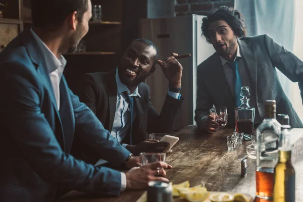 Homens Multiétnicos Sorridentes Conversando Bebendo Uísque Fumando Charutos Enquanto Festejam — Fotografia de Stock