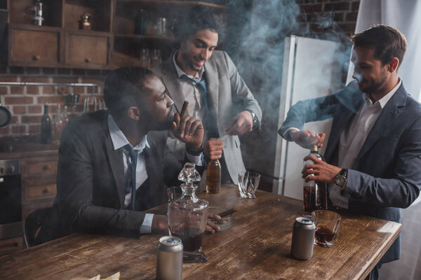 young multiethnic businessmen smoking cigars and drinking alcoholic beverages