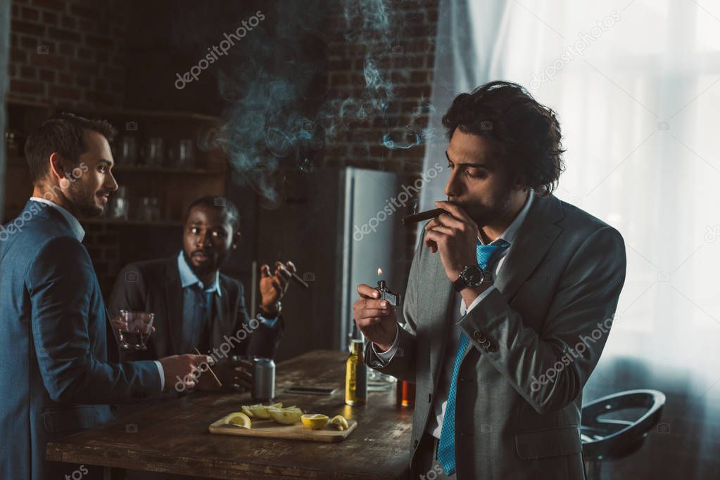 handsome young businessman smoking cigar while friends drinking whiskey behind 