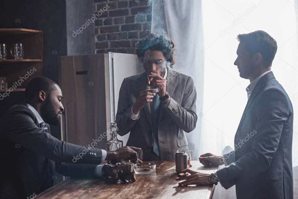 young multiethnic businessmen smoking cigars and drinking alcohol together