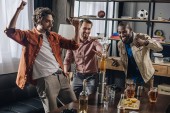 Veselá mnohonárodnostní muži přátelé baví a zatímco párty doma při pohledu na věž od lahví a sklenic