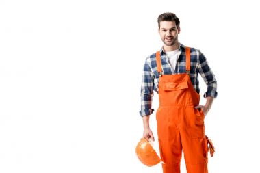 Smiling handyman in orange overall holding hard hat isolated on white clipart