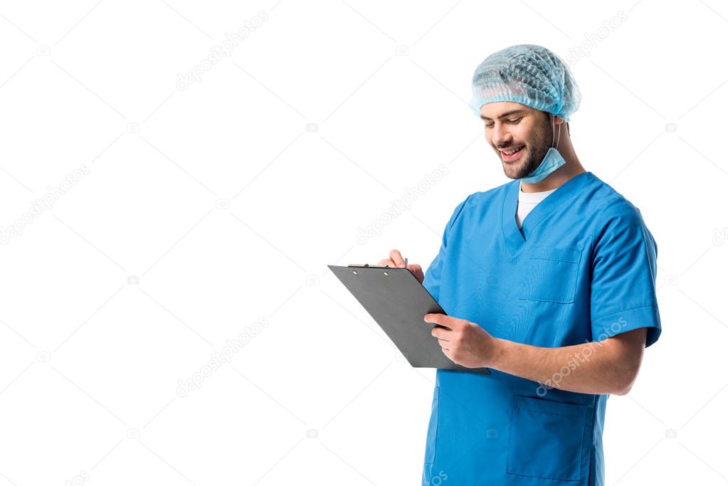 Cheerful surgeon  wearing blue uniform and holding clipboard isolated on white