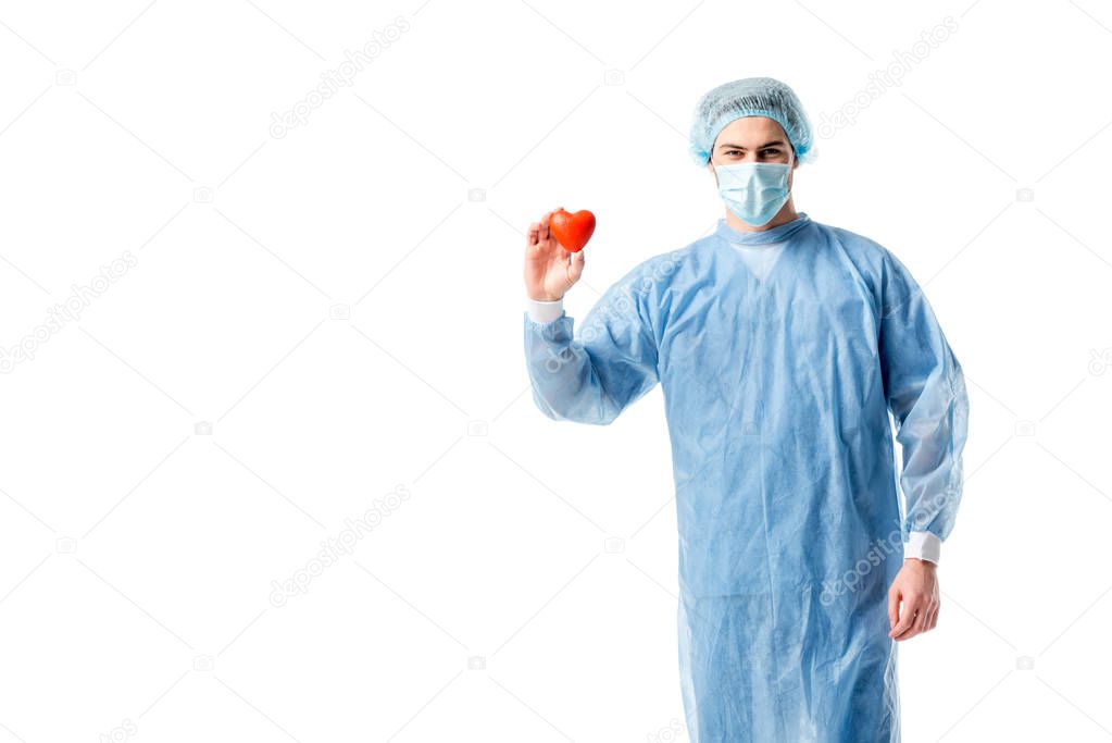 Man wearing blue medical uniform and medical mask and holding toy heart isolated on white
