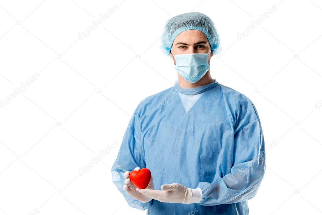 Surgeon in blue medical uniform and medical mask and holding toy heart isolated on white