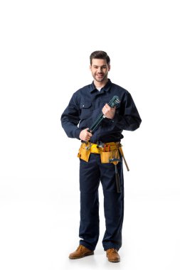 Confident handyman wearing uniform with tool belt and holding wrench isolated on white clipart