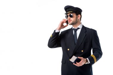 Pilot üniformalı pasaport ve bilet elinde beyaz izole smartphone cep telefonu ile konuşmak